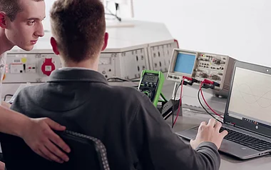 Techniker analysiert Schaltkreise mit Messgeräten und Laptop.