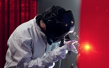Schweißer führt eine Schweißnaht mit Schutzbrille und Handschuhen aus.