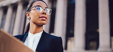 Eine Fachfrau hält eine Akte vor einem repräsentativen Gebäude.