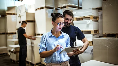 Mitarbeiter überprüfen Daten auf einem Tablet in einem Lagerraum.