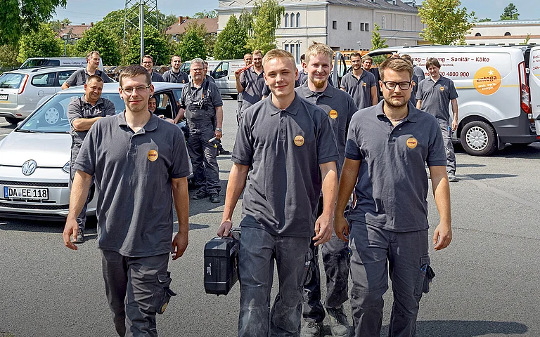Monteure tragen Werkzeug und gehen auf einen Parkplatz.