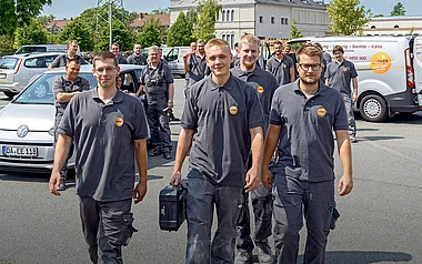 Monteure tragen Werkzeug und gehen auf einen Parkplatz.