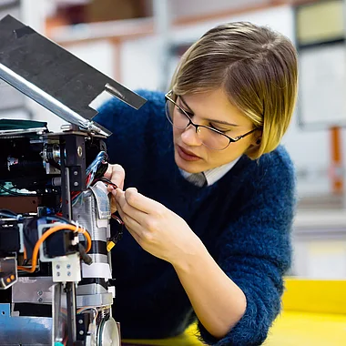 Eine Technikerin repariert elektronische Bauteile mit Werkzeug.