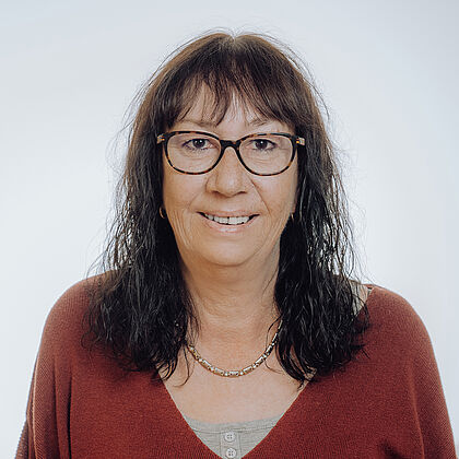 Frau mit Brille und braunem Pullover lächelt freundlich in die Kamera.