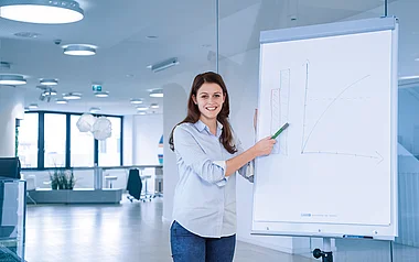 Junge Frau präsentiert Diagramm an einer Whiteboard in einem modernen Büro.