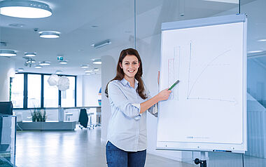 Junge Frau präsentiert Diagramm an einer Whiteboard in einem modernen Büro.