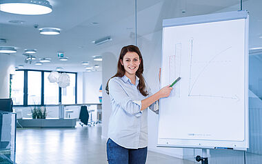 Junge Frau präsentiert Diagramm an einer Whiteboard in einem modernen Büro.