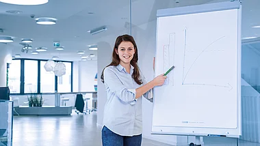 Junge Frau präsentiert Diagramm an einer Whiteboard in einem modernen Büro.