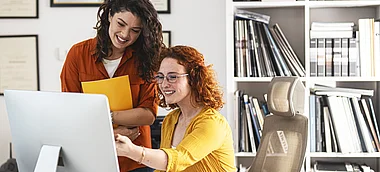 Zwei Frauen besprechen Inhalte auf einem Bildschirm in einem Büro.