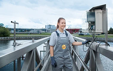 Mitarbeiterin inspiziert eine Kläranlage mit technischer Ausrüstung im Hintergrund.