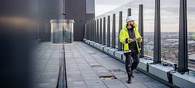 Bauarbeiter inspiziert Dach eines modernen Bürogebäudes. Blick auf die Stadt im Hintergrund.