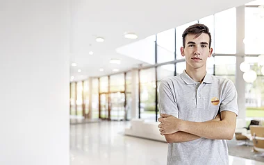 Ein Mann in grauem Poloshirt steht lächelnd vor einer Glaswand.