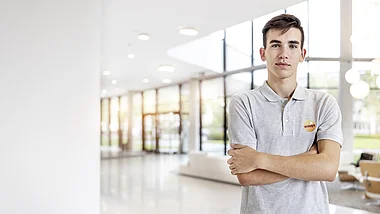 Ein Mann in grauem Poloshirt steht lächelnd vor einer Glaswand.