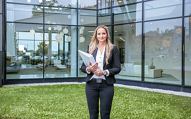 Eine Geschäftsfrau hält eine Akte vor einem modernen Bürogebäude.
