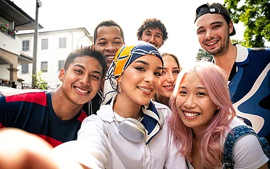 Eine Gruppe junger Menschen posiert lächelnd vor einem Stadtgebäude.