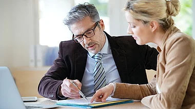 Zwei Fachleute besprechen Dokumente und Diagramme bei einer Präsentation.