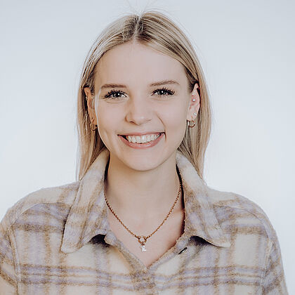 Eine lächelnde Frau trägt ein kariertes Hemd.