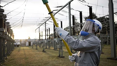 Techniker inspiziert Strommasten bei Sonnenuntergang.