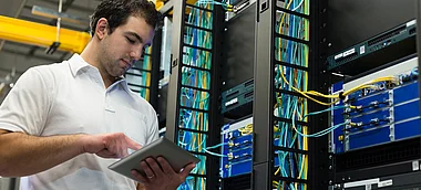 Techniker inspiziert Serverracks mit einem Tablet in einem Rechenzentrum.