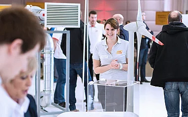 Mitarbeiterin präsentiert ein Modell einer Windkraftanlage auf einer Messe.
