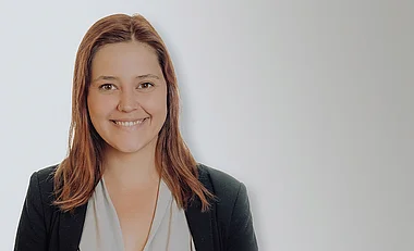 Frau in Blazer, lächelnd und professionell für ein Porträt.